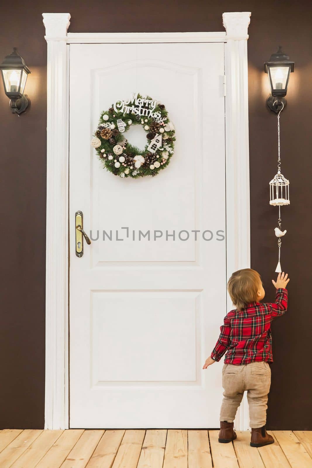 adorable baby stands at the front door with a christmas wreath.
