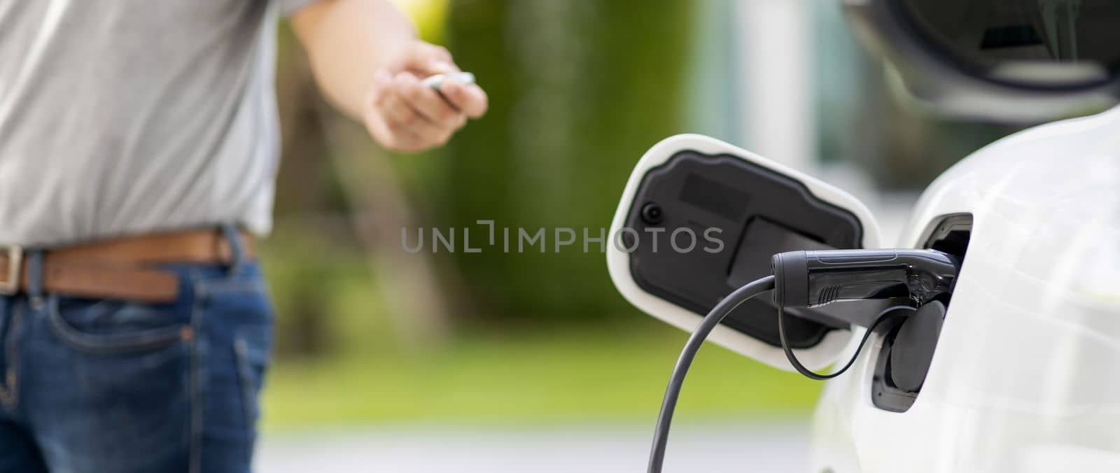 Focus recharging electric vehicle outdoor from charging station with blurred background of man at EV car. Concept ideal for new progressive technology of green and renewable energy for car.