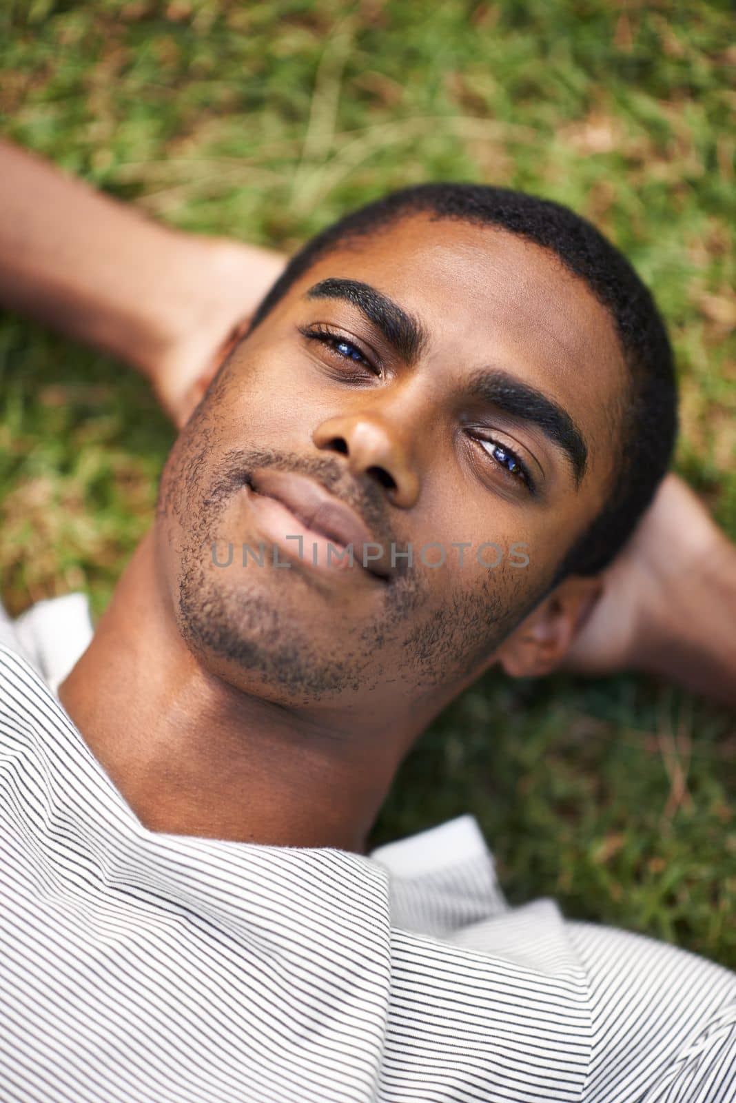 Taking in the sunshine. a handsome young man lying on the grass outdoors. by YuriArcurs