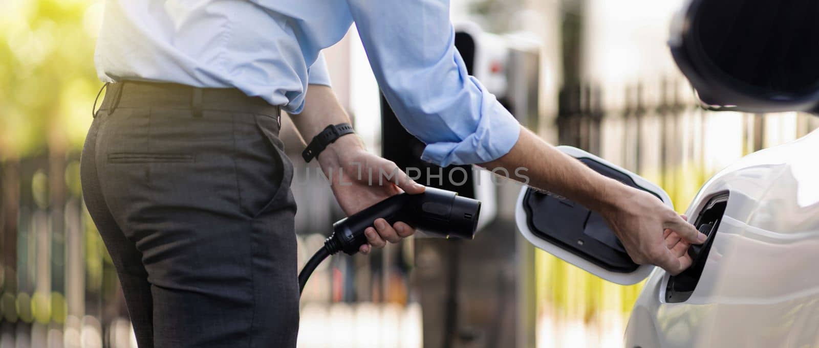 Closeup progressive man holding EV charger plug from public charging station for electric vehicle with background of residential building as concept eco-friendly sustainability energy car concept.