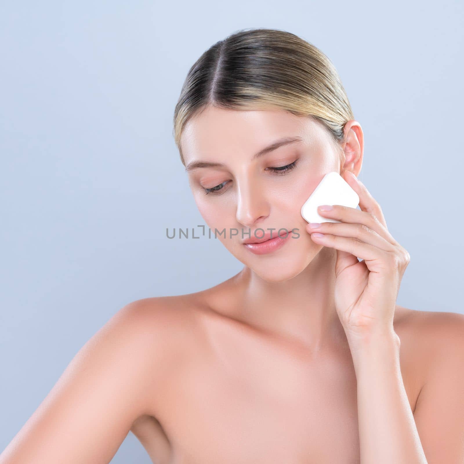 Alluring beautiful female model applying powder puff for facial makeup concept. Portrait of flawless perfect cosmetic skin woman put powder foundation on her face in isolated background.