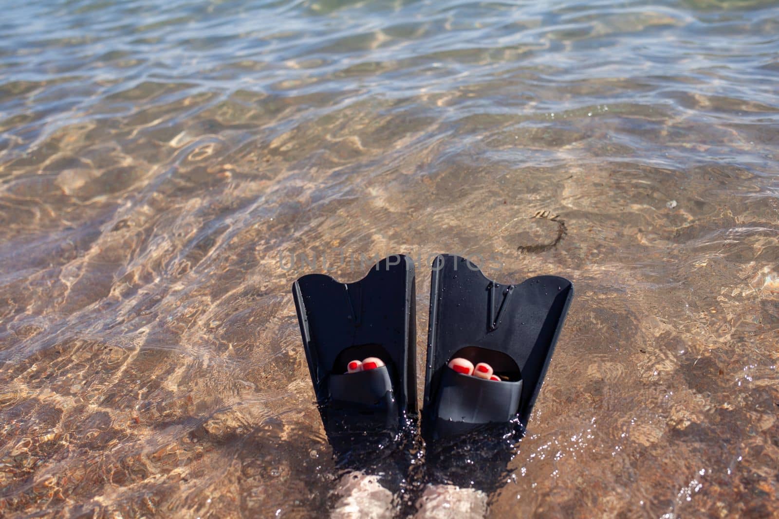 A woman in black flippers splashes near the shore. Fins stick out of the water. Swimming equipment. Summer holidays, fun, exploring the sea world concept. Space for copy.