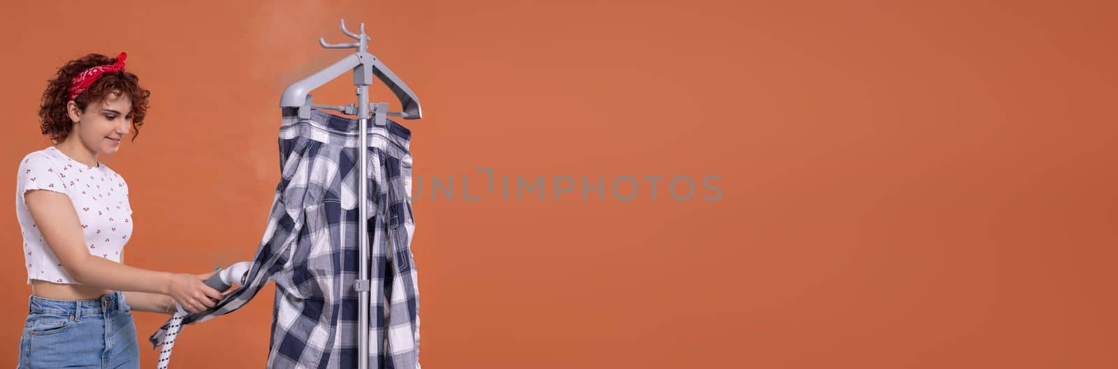 Panoramic frame of young girl. Smiling girl using a steamer to iron a man's shirt. Attractive girl with dark and curly hair. Hot steam.