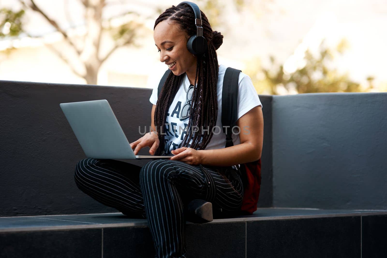 Blogging outdoors is always fun. an attractive young woman listening to music and using her laptop while relaxing outdoors. by YuriArcurs