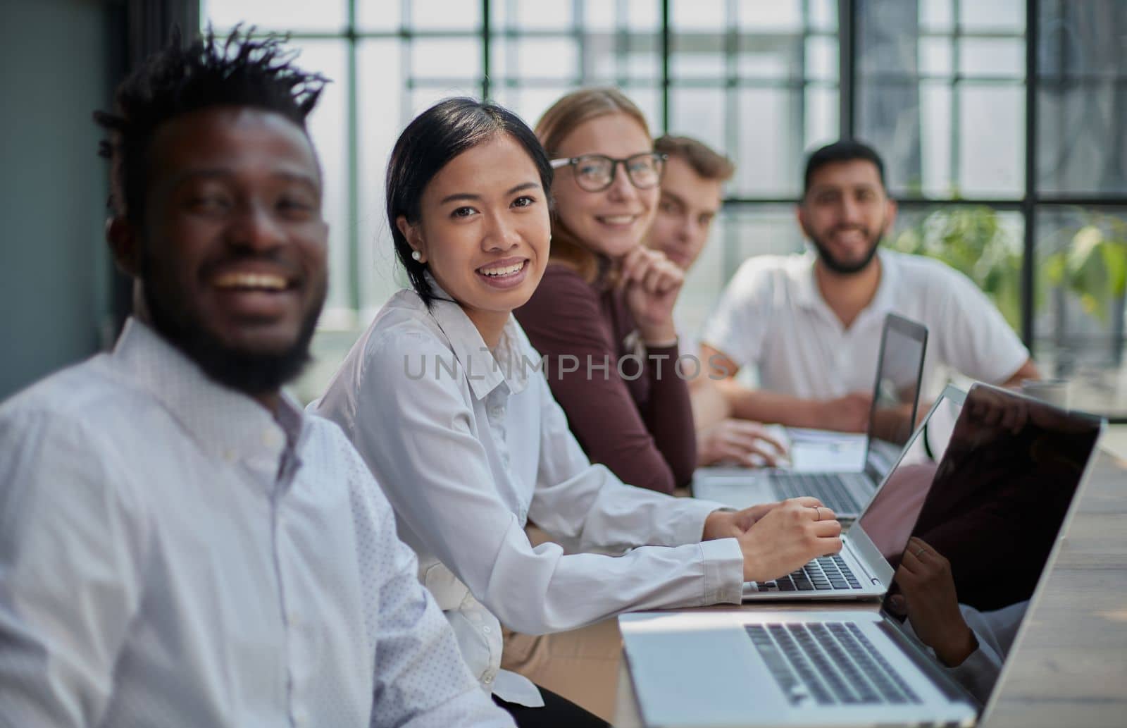 Multicultural colleagues sitting at desk near digital devices and documents during business meeting