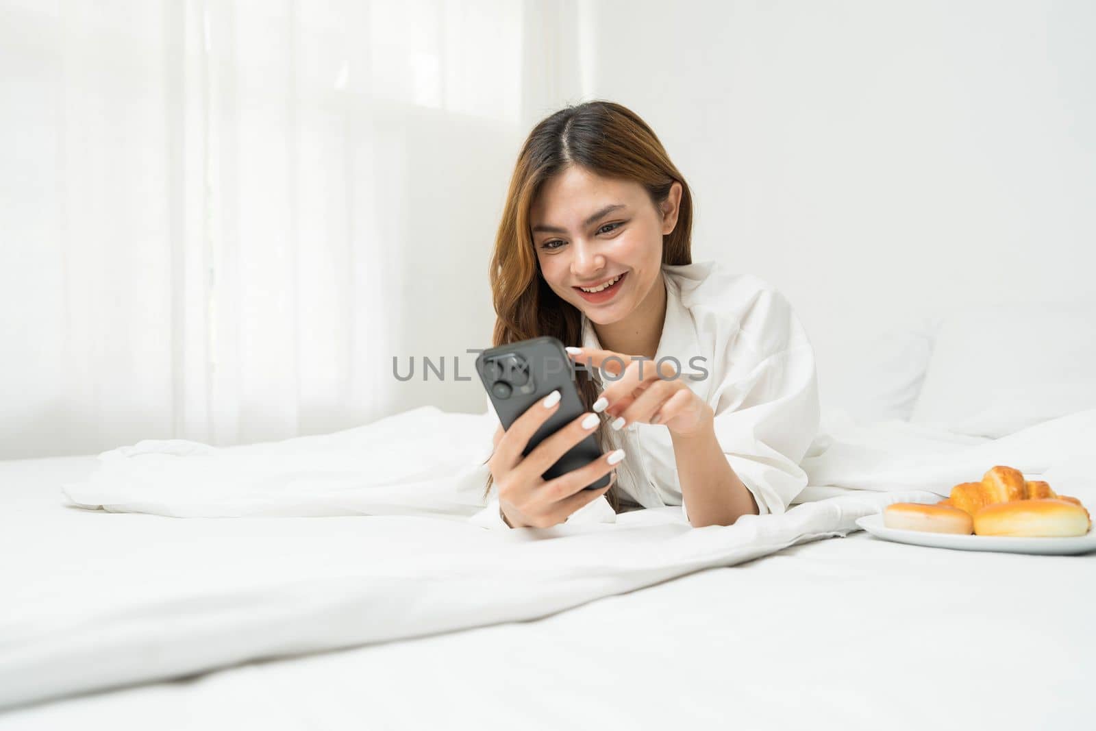 Beautiful young asian woman smiling sitting relax on the bed in the morning, girl using mobile smart phone talking enjoy, communication and social network concept. by wichayada