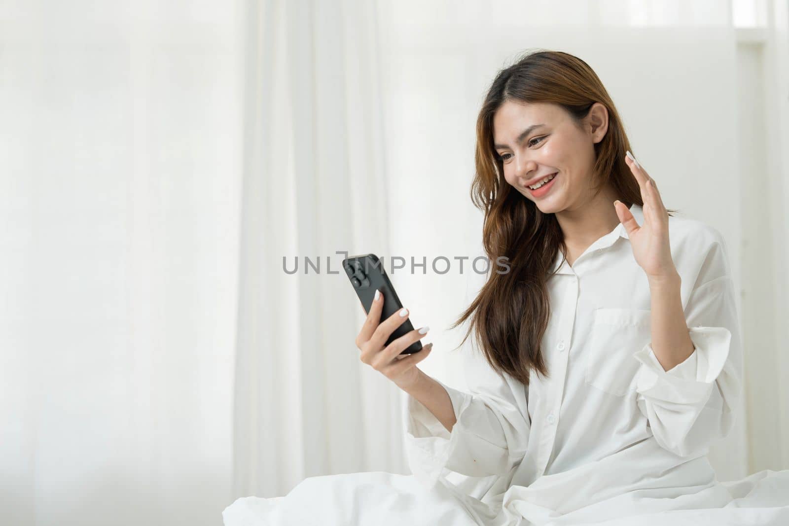 Beautiful young asian woman smiling sitting relax on the bed in the morning, girl using mobile smart phone talking enjoy, communication and social network concept. by wichayada