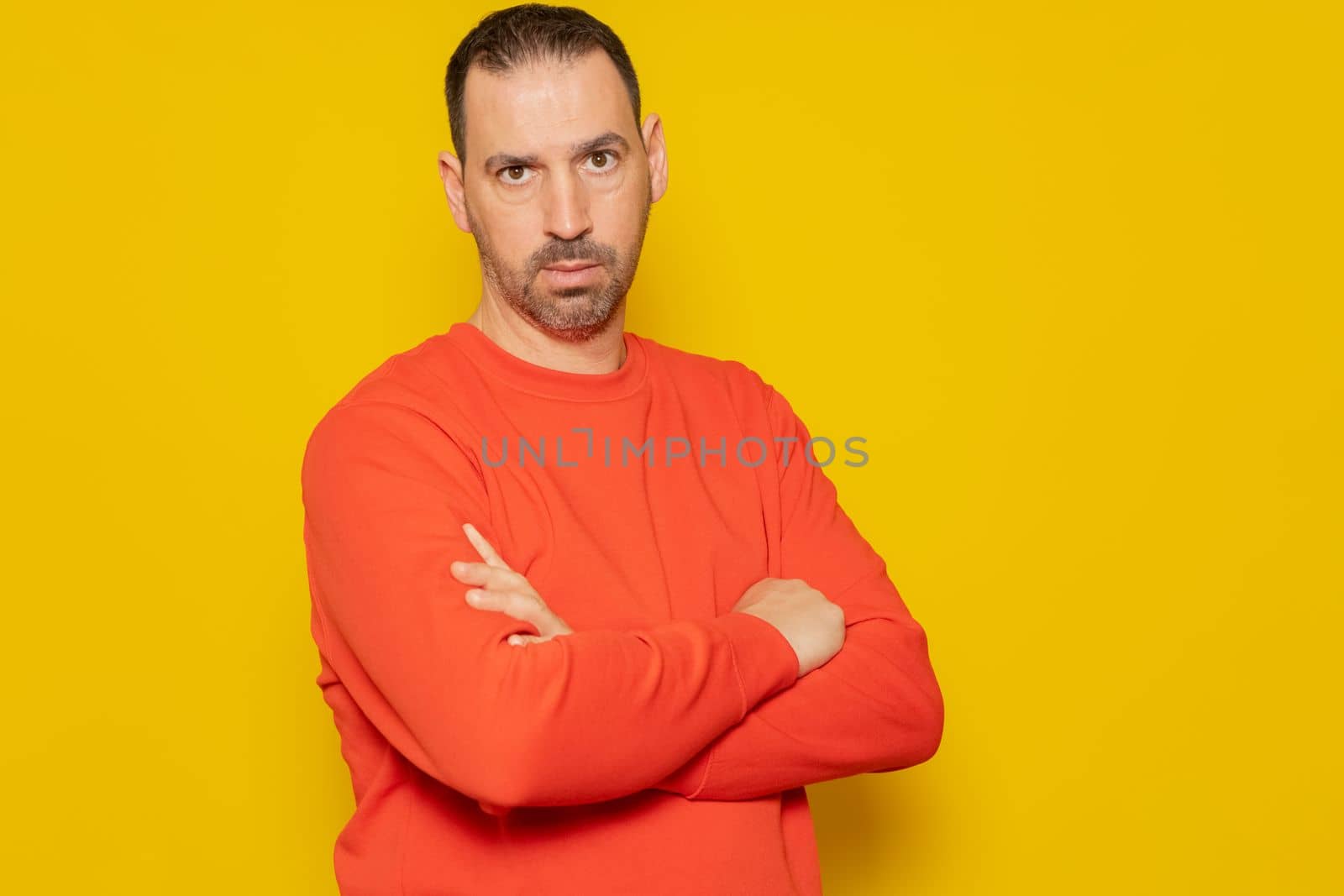 Bearded latino man wearing a red sweater with crossed arms isolated over yellow background, he is furious and angry as he can't get his followers up on social networks