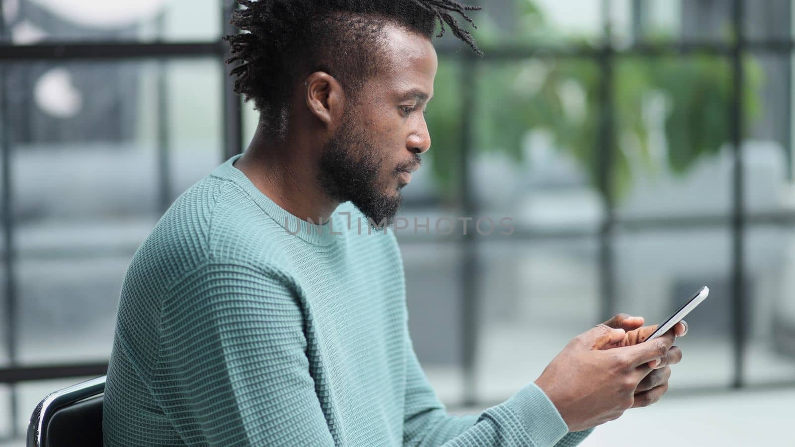 Black man looking at smartphone browsing internet, office technology and digital communication