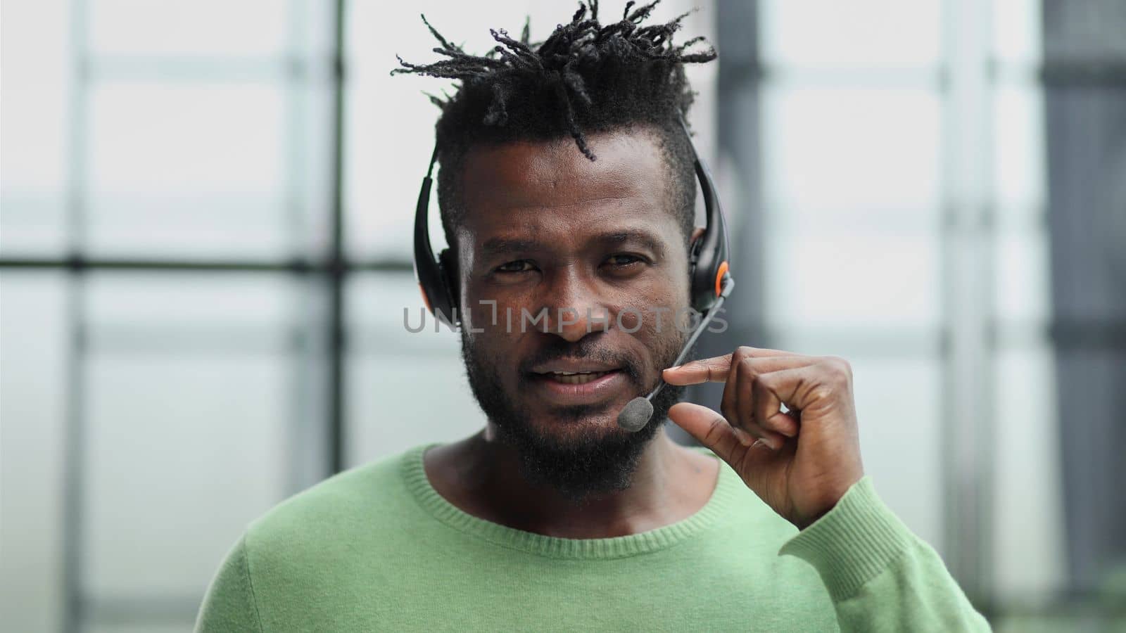 Operator of hot line. Portrait of cheerful african customer service representative with headset in call center, empty space