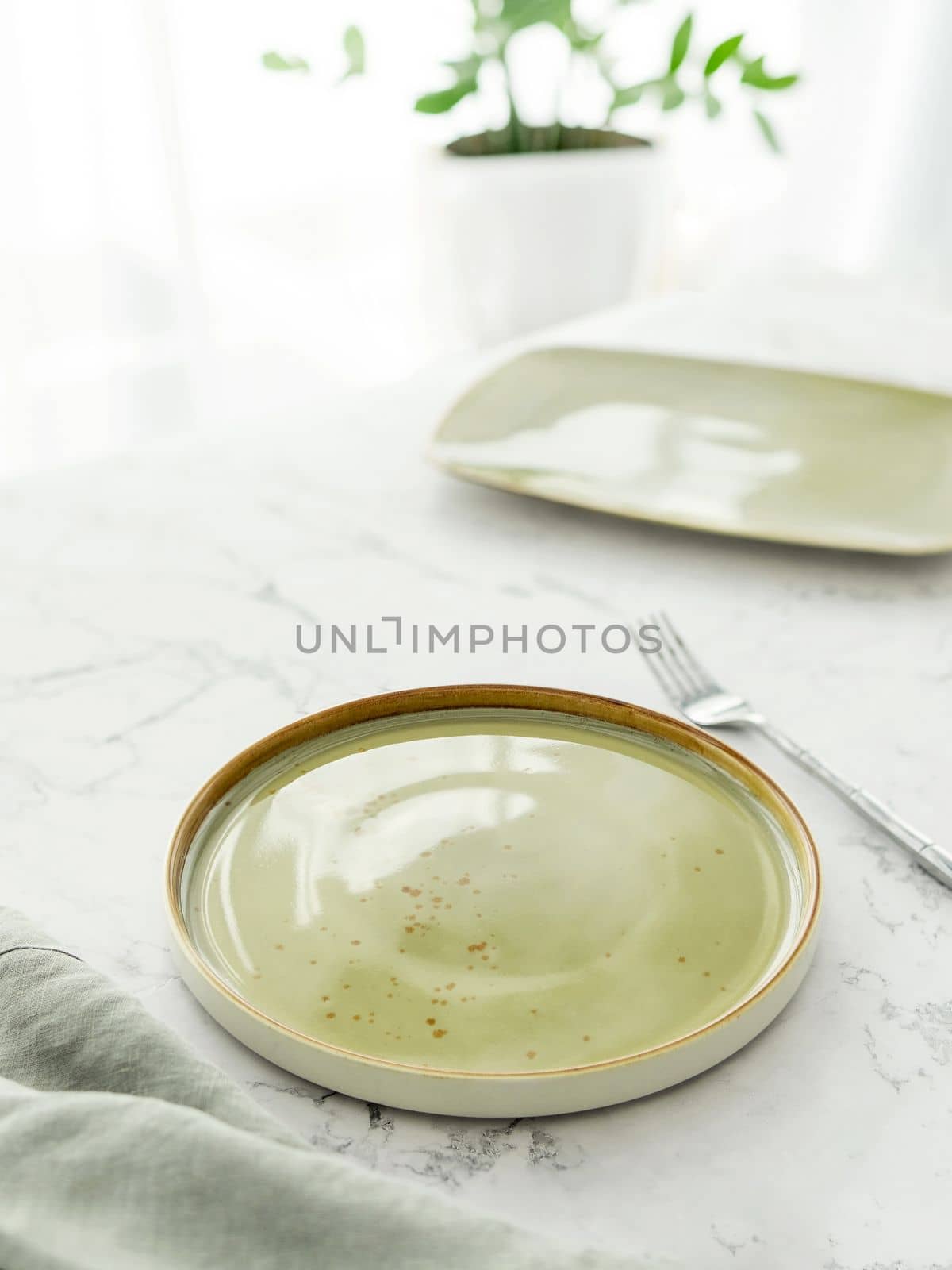 Empty green plate with tablecloth and fork on white marble table in front of window
