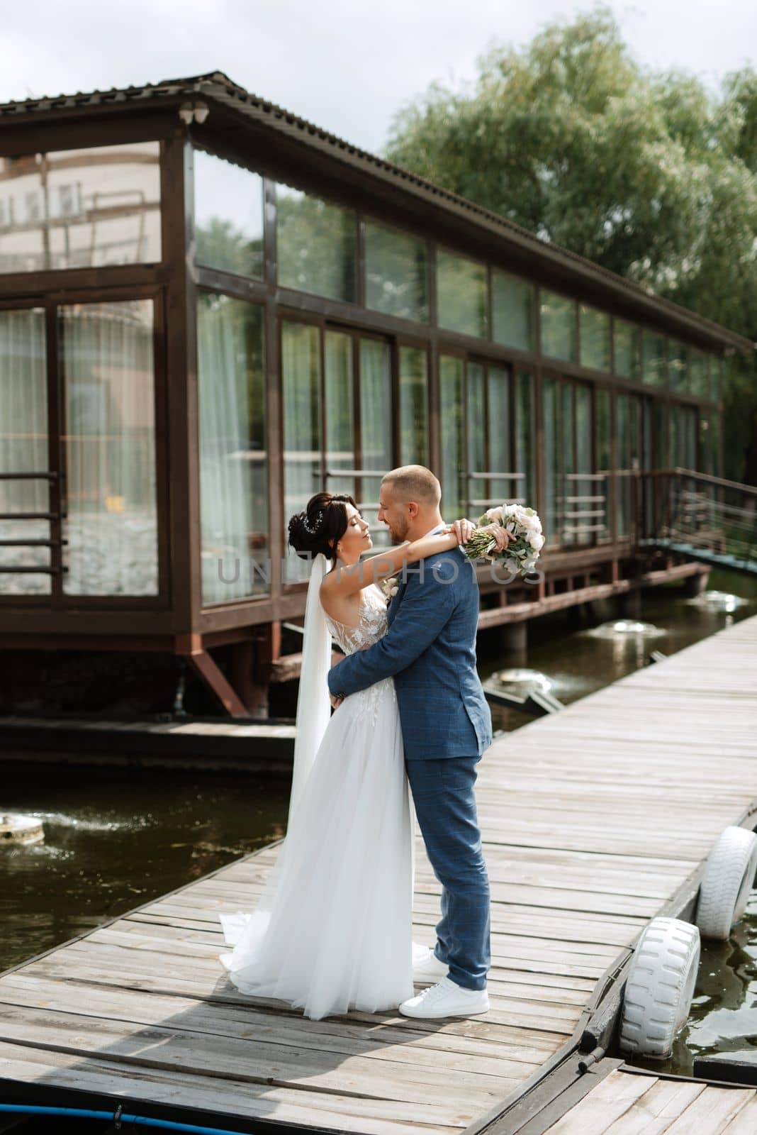 the first meeting of the bride and groom in wedding dresses on the pier near the water