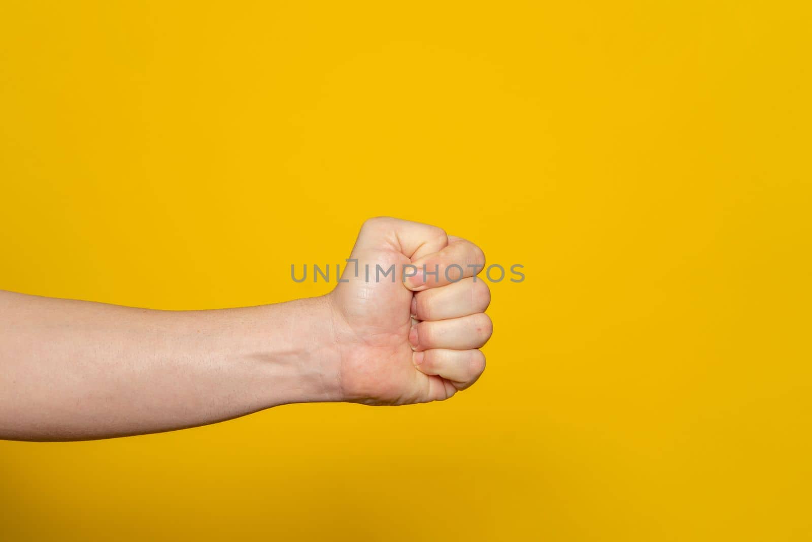 Strong man's hand in the form of a fist horizontally, isolated on yellow background. Fist ready to hit and hurt