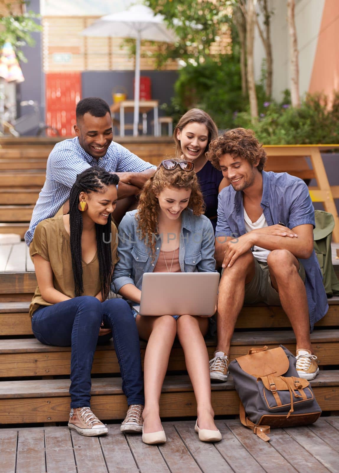 Lets take this lesson online. A group of students gathered around a laptop outdoors. by YuriArcurs