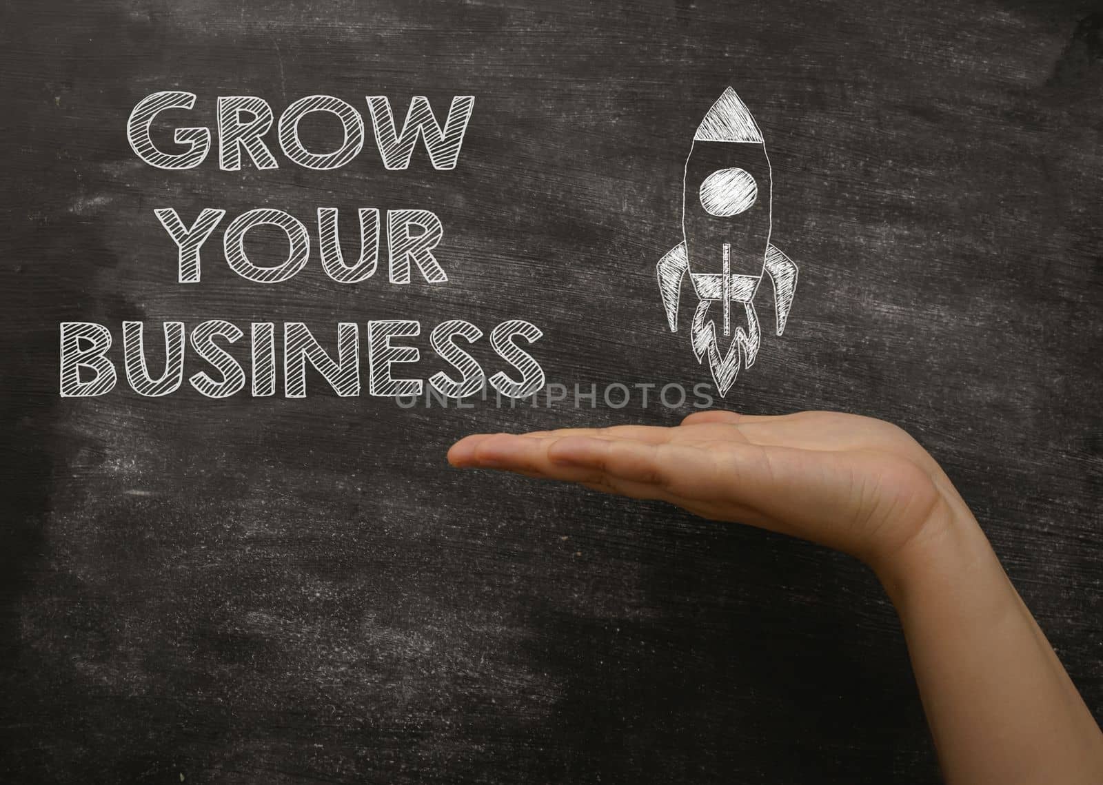 Person palm points to phrase Grow Your Business and rocket picture on blackboard. Step-by-step guide to get more customers to business company