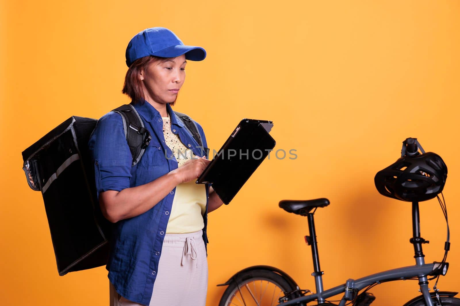 Concentrated elderly deliverywoman holding digital device checking client location by DCStudio