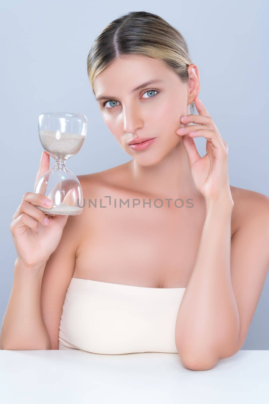 Alluring beauty model using hourglass in beauty concept of anti-aging skincare treatment for woman. Beautiful caucasian women portrait with perfect smooth clean skin in isolated background.