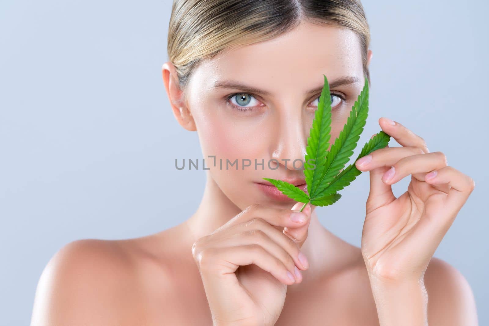 Closeup alluring beautiful woman model portrait holding green leaf as concept for cannabis skincare cosmetic product for skin freshness treatment in isolated background.