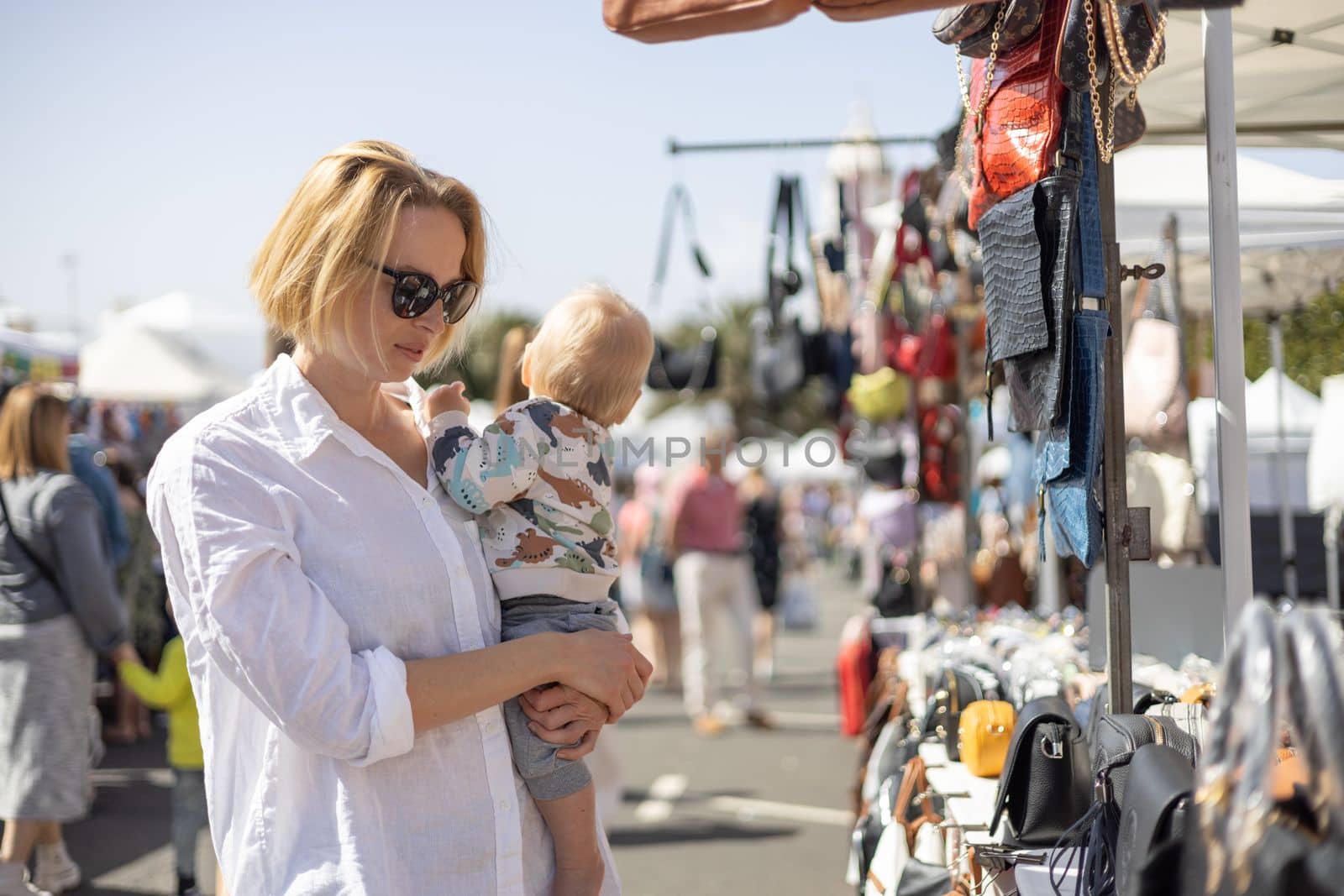 Mother hoding his infant baby boy child whilechecing items at sunday flea market. by kasto