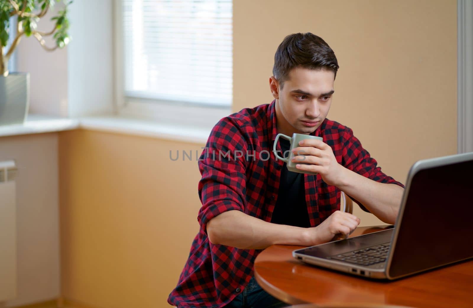 Handsome man working using computer laptop and drinking a cup of coffee at home