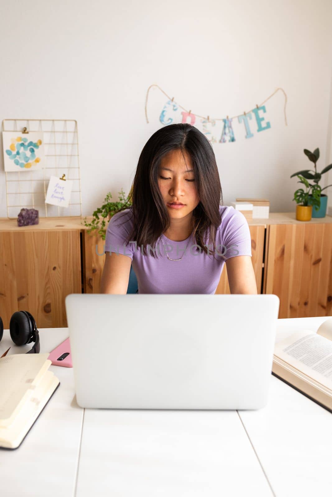 Vertical portrait of teenage female Asian high school student doing homework and studying at home using laptop. Education and technology concepts.