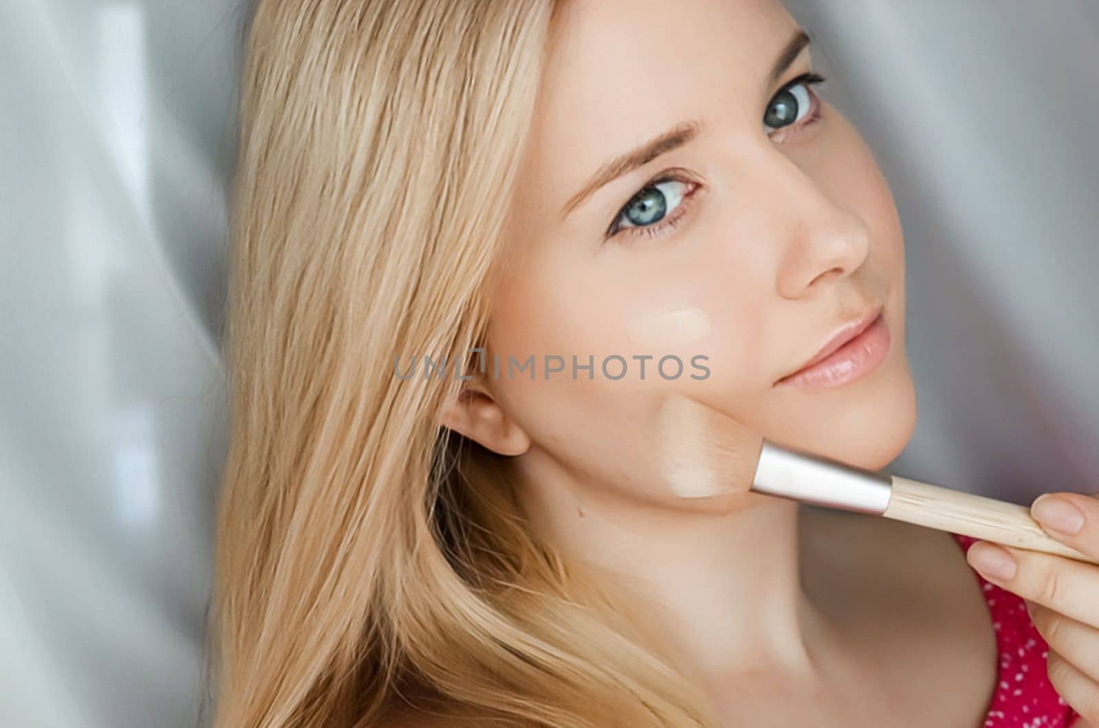 Beautiful blonde woman applying liquid make-up foundation on her skin with make-up brush by Anneleven