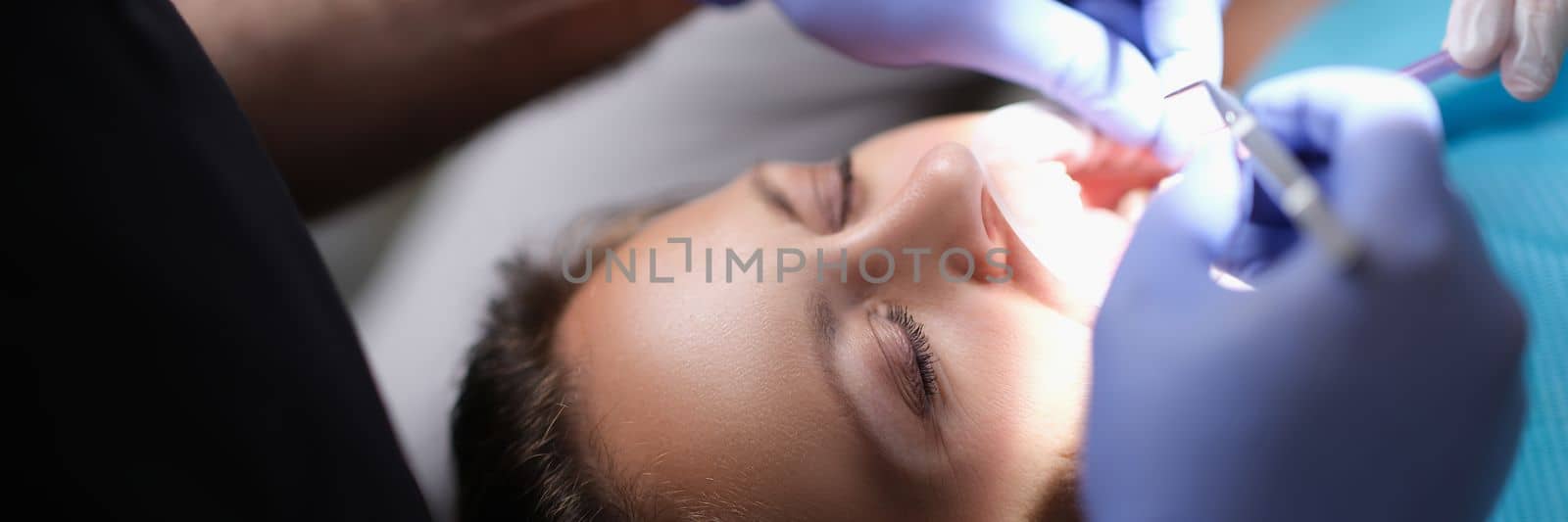 Dentist examines patient teeth at dentist and dental instrument. Doctor examines oral cavity of female patient