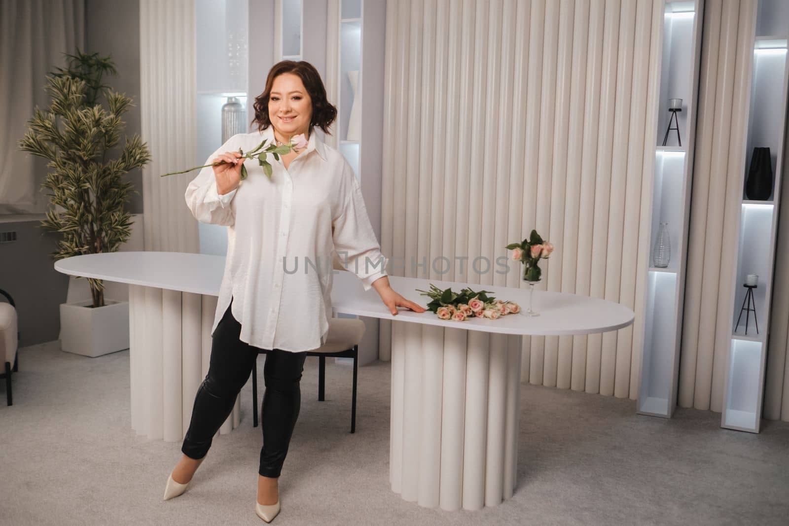 An adult woman in a white shirt holds one rose in her hands while standing in the interior. Pink roses.