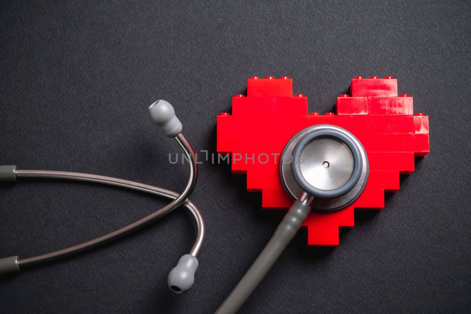 stethoscope standing on red heart on dark gray background by Sonat