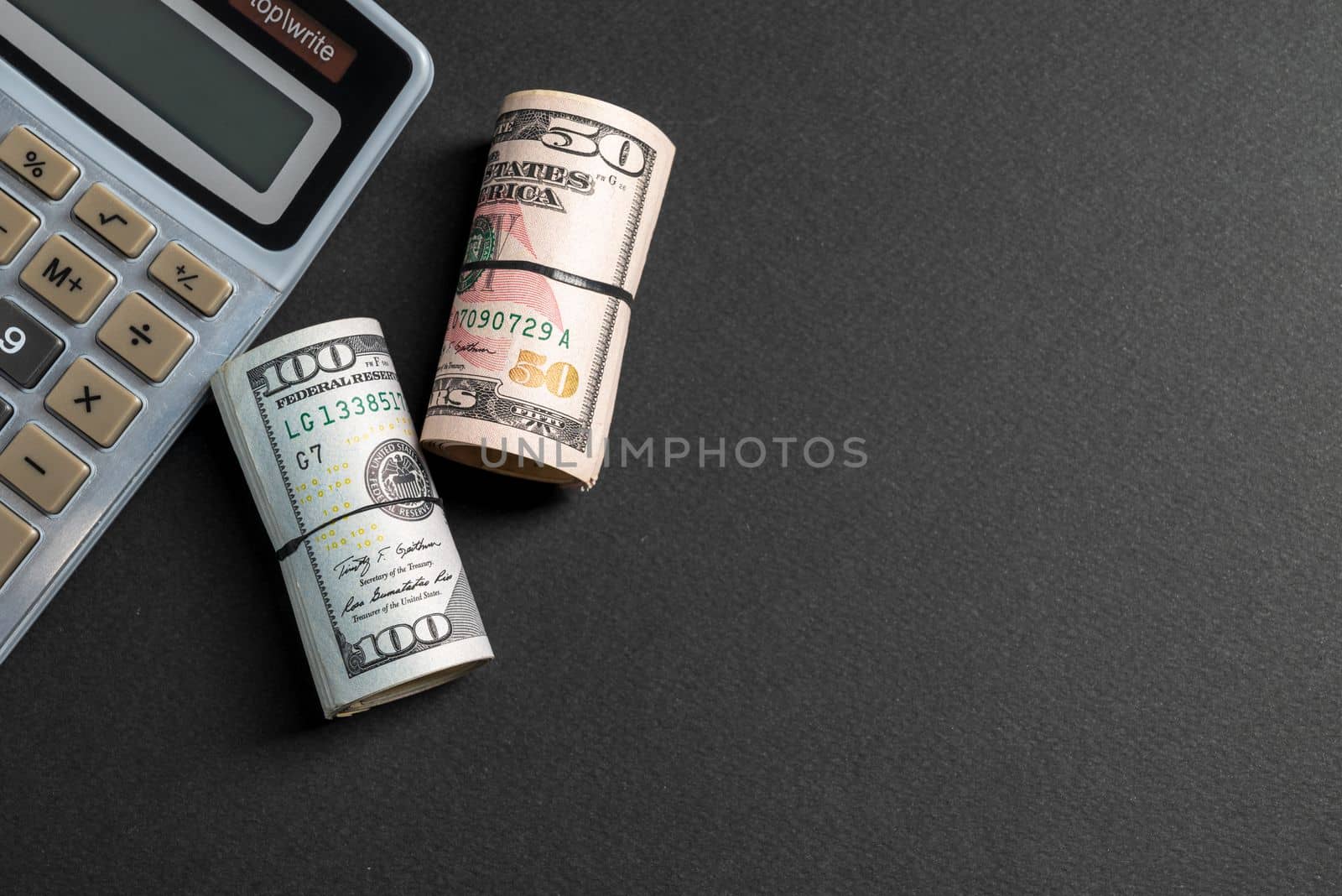 Rolls of 50 and 100 us dollar standing near calculator on dark background