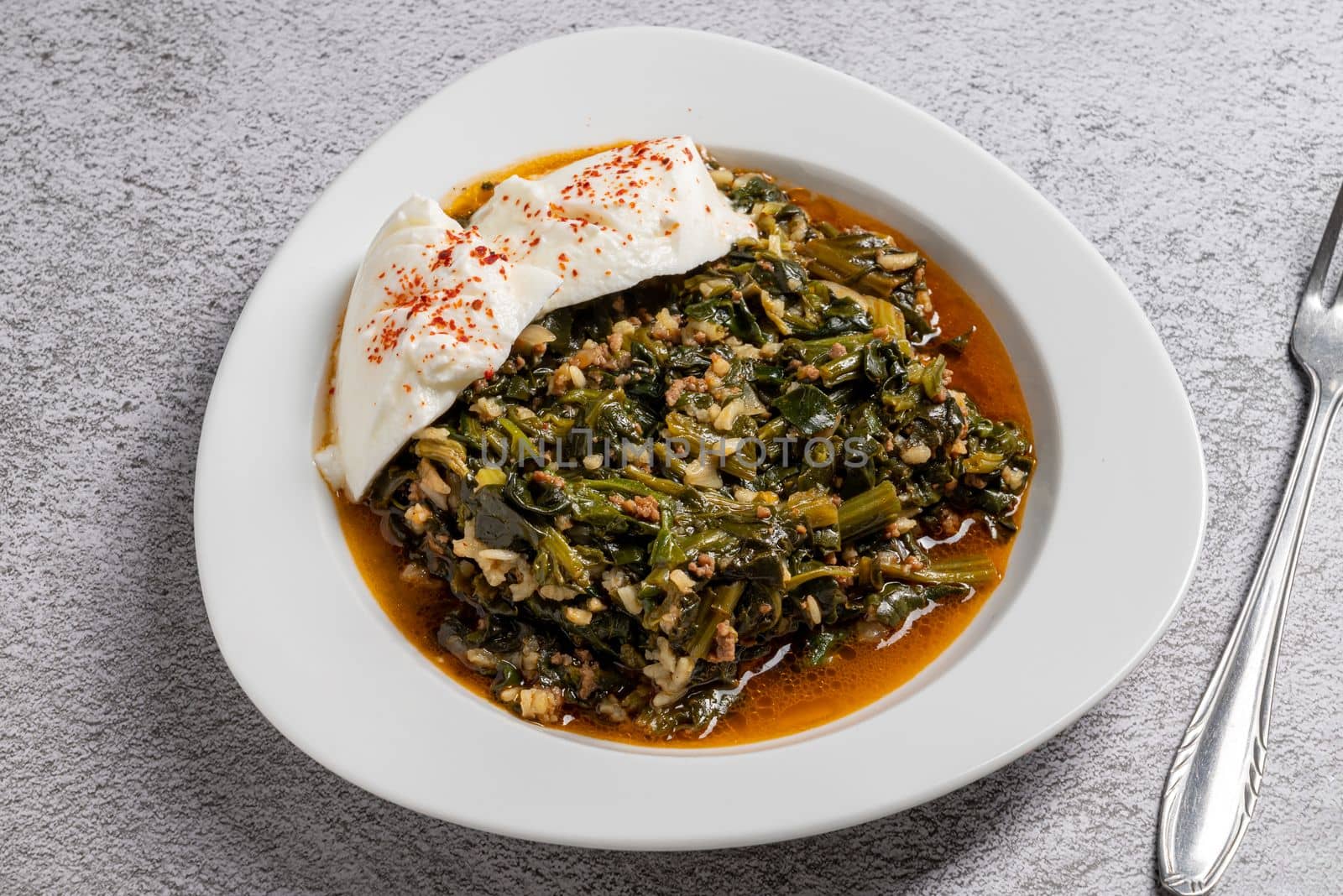 Traditional Turkish spinach meal with rice and minced meat with yogurt on a white porcelain plate