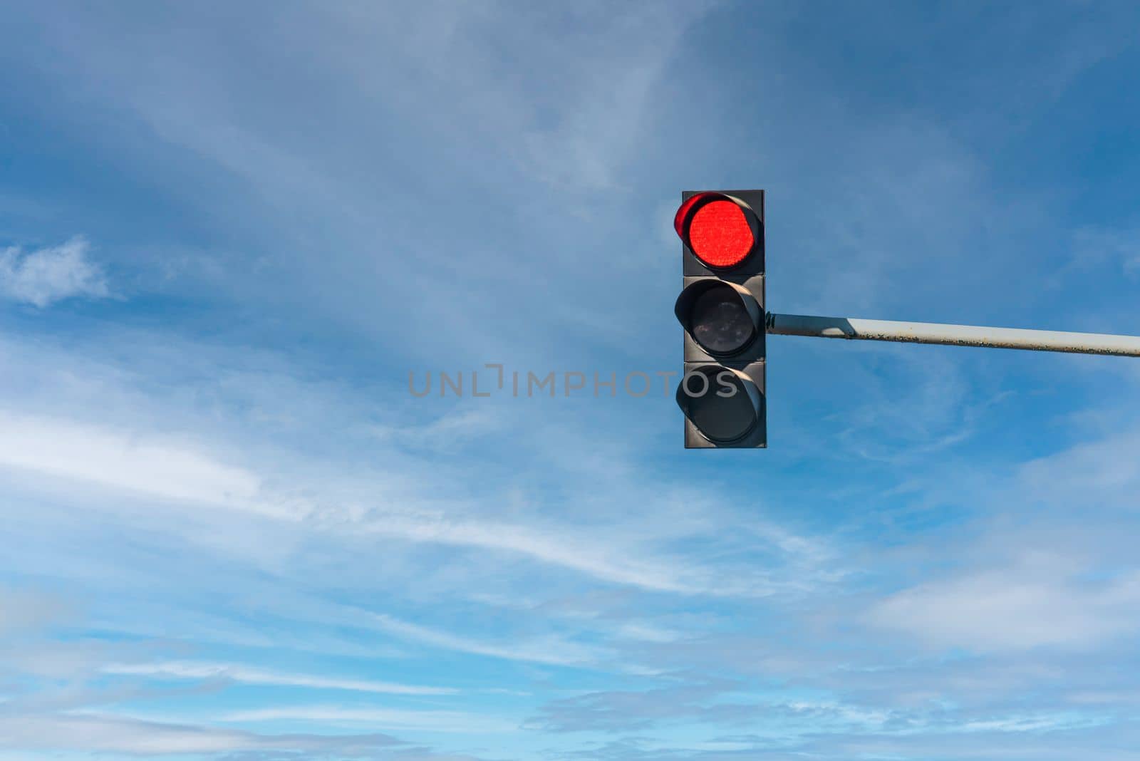 Modern traffic light with red light in front of cloudless sunny blue sky