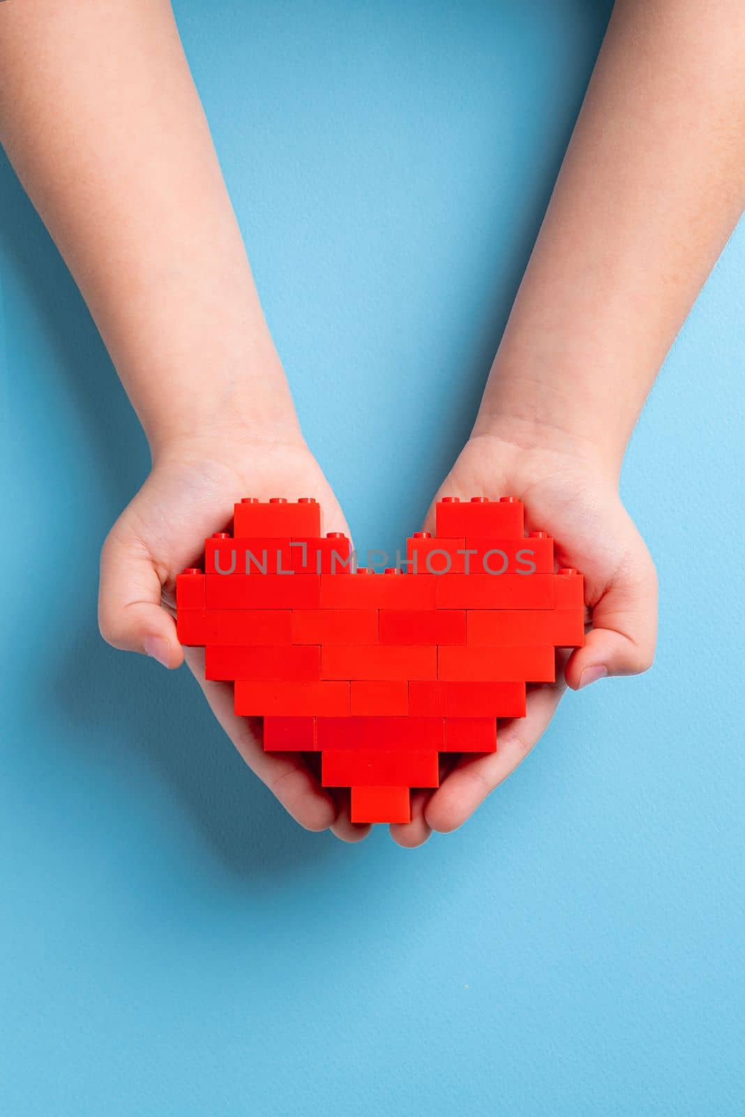 Hands of little girl child holding heart made of plastic bricks on blue background by Sonat