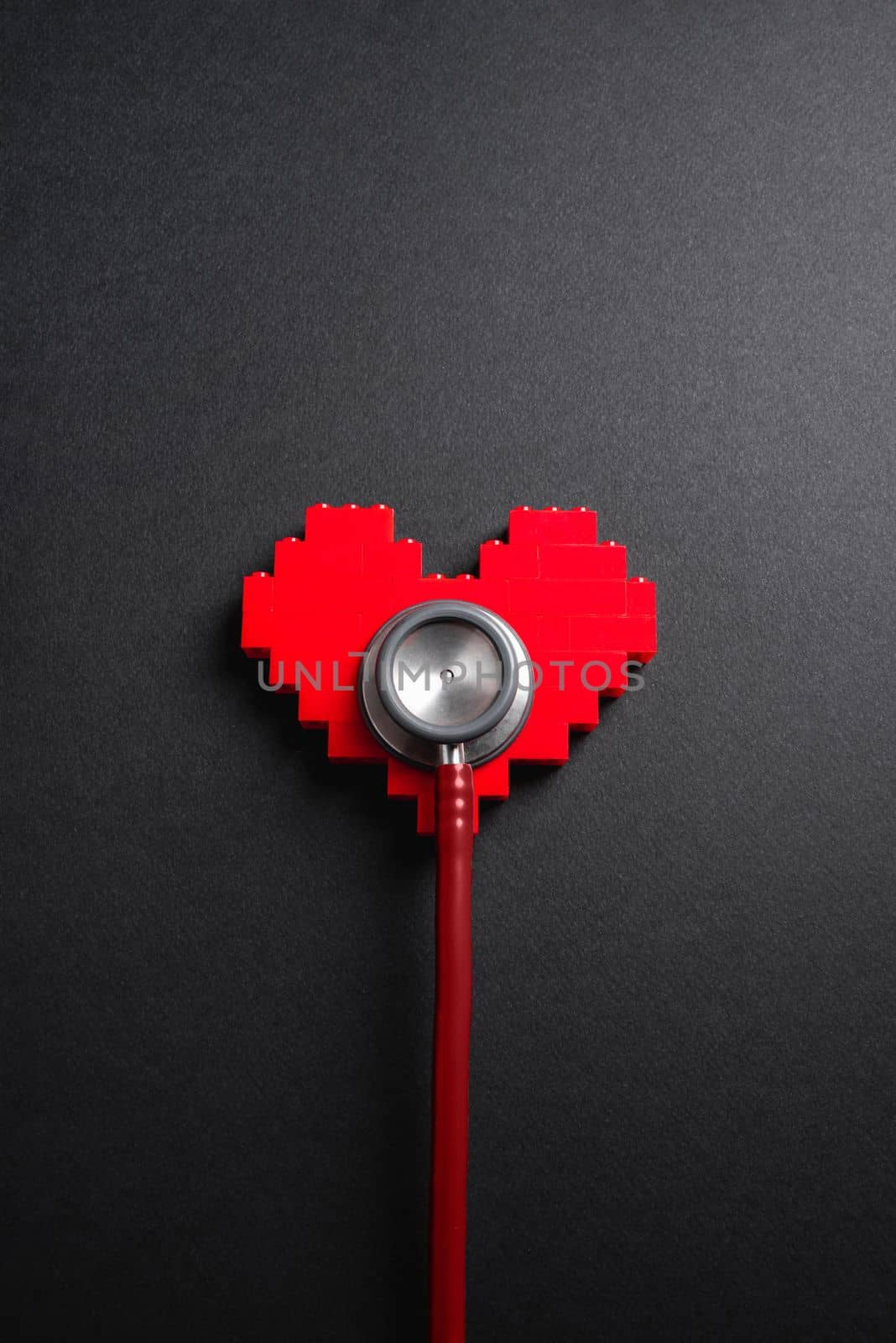 Red stethoscope standing on red heart on dark gray background by Sonat