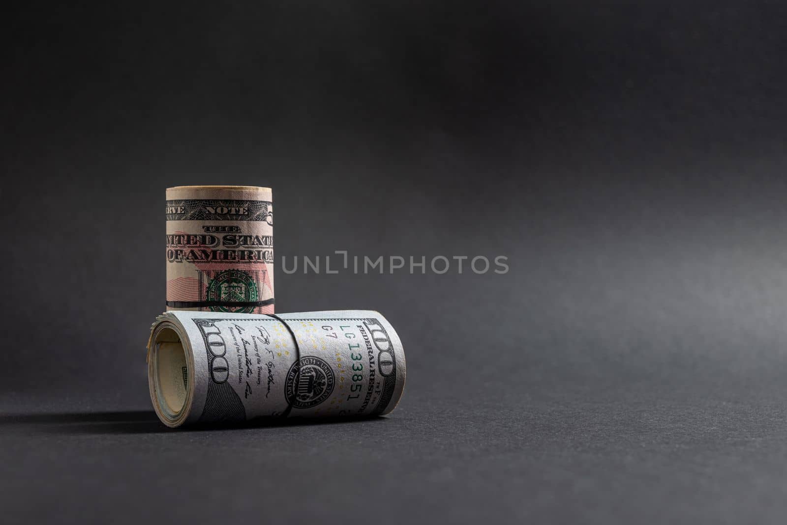 Rolls of 50 and 100 us dollar standing on dark background