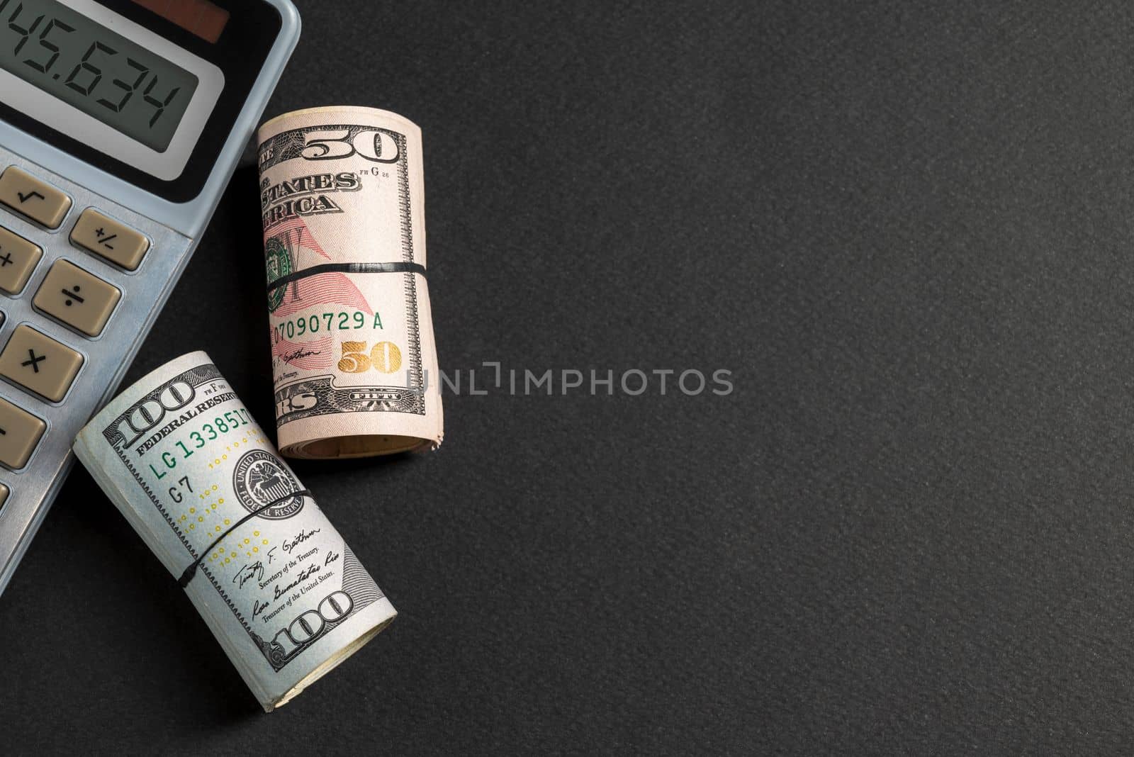 Rolls of 50 and 100 us dollar standing near calculator on dark background