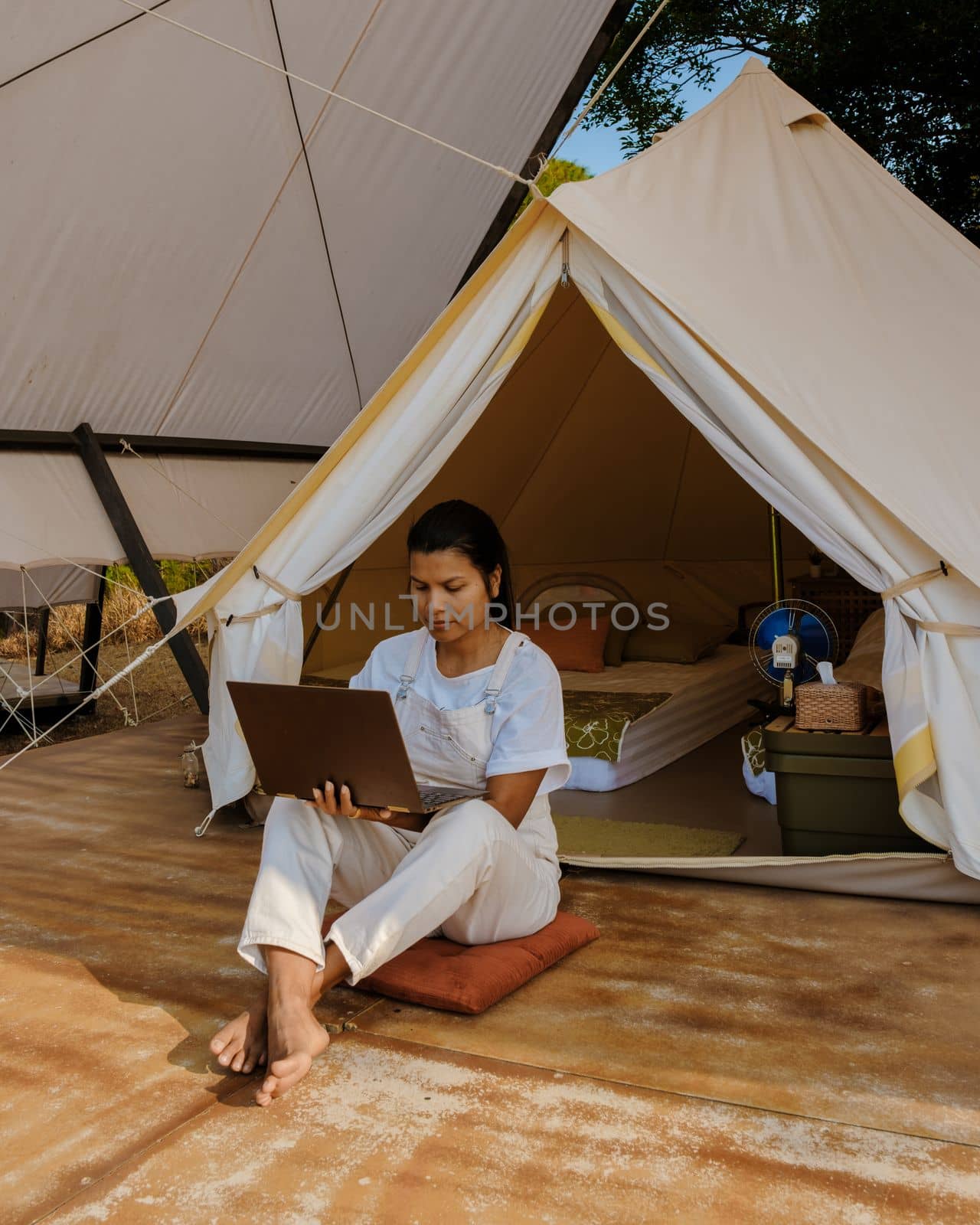 Young woman freelancer working online using a laptop in front of a tent in the mountains by fokkebok