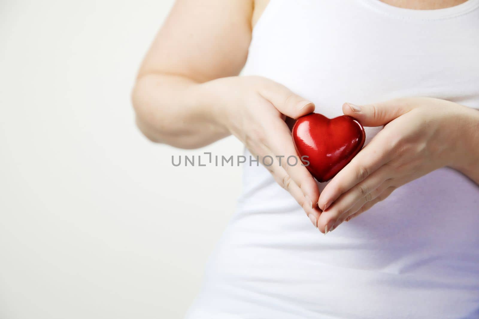 health, medicine and charity concept close up of female hands with small red heart holding for breast on white background copy space awareness