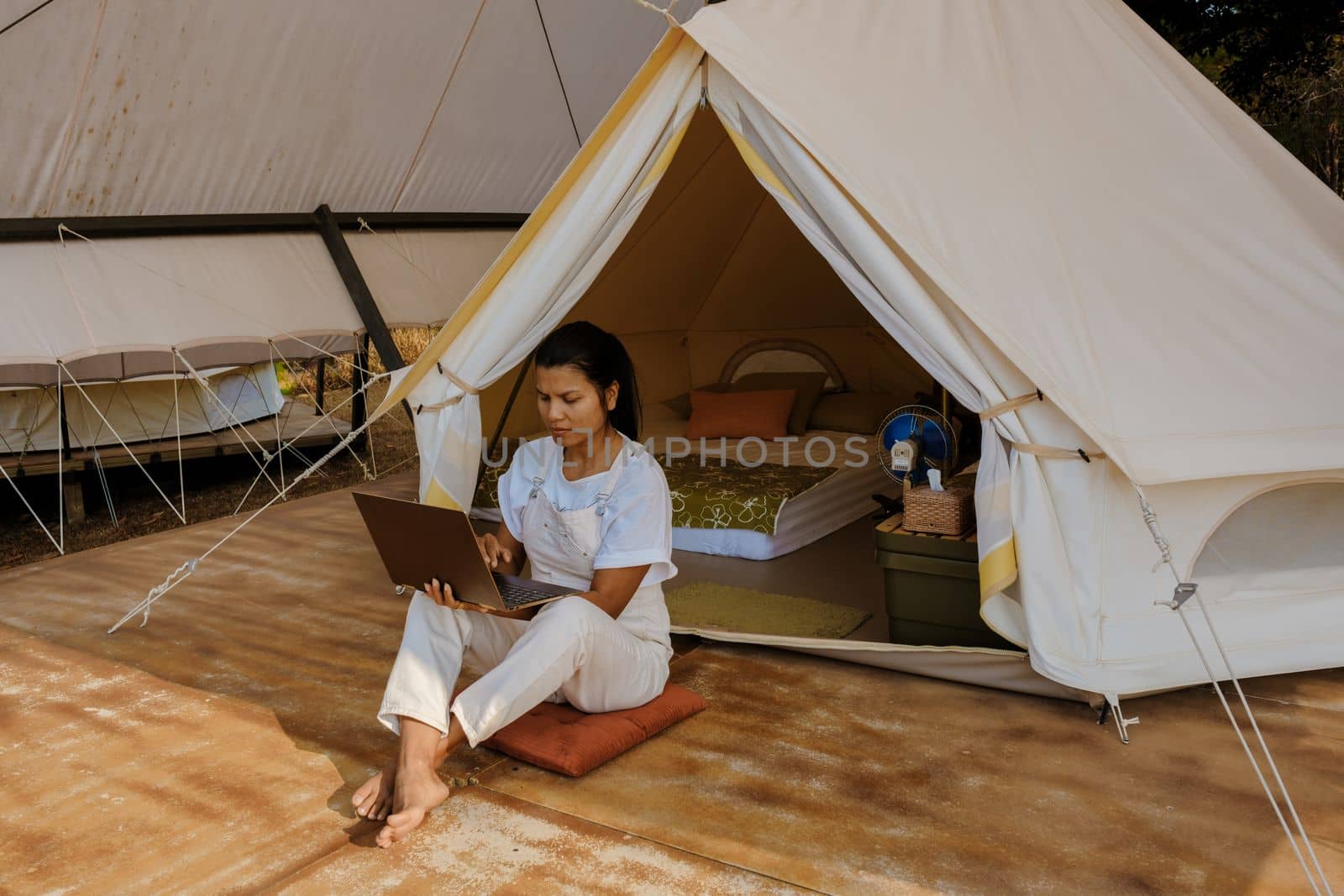 Young Asian woman freelancer working online using a laptop in front of a tent in the mountains by fokkebok