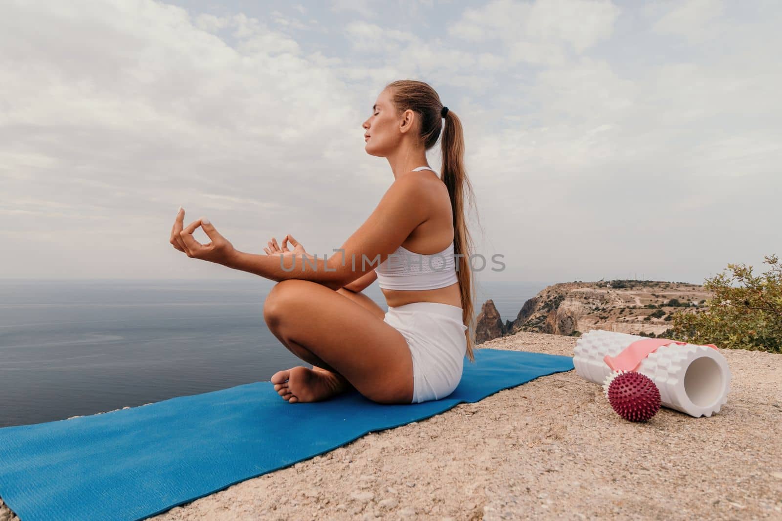 Middle aged well looking woman with black hair doing Pilates with the ring on the yoga mat near the sea on the pebble beach. Female fitness yoga concept. Healthy lifestyle, harmony and meditation.