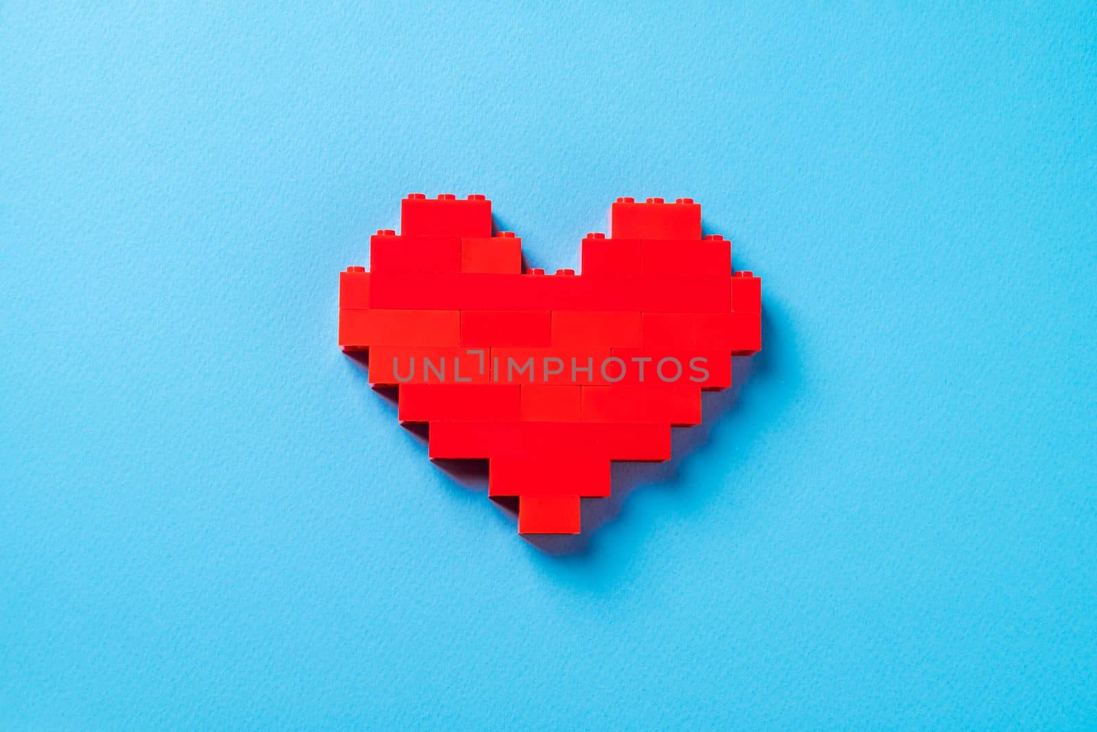 Red heart made of plastic bricks on a blue background by Sonat