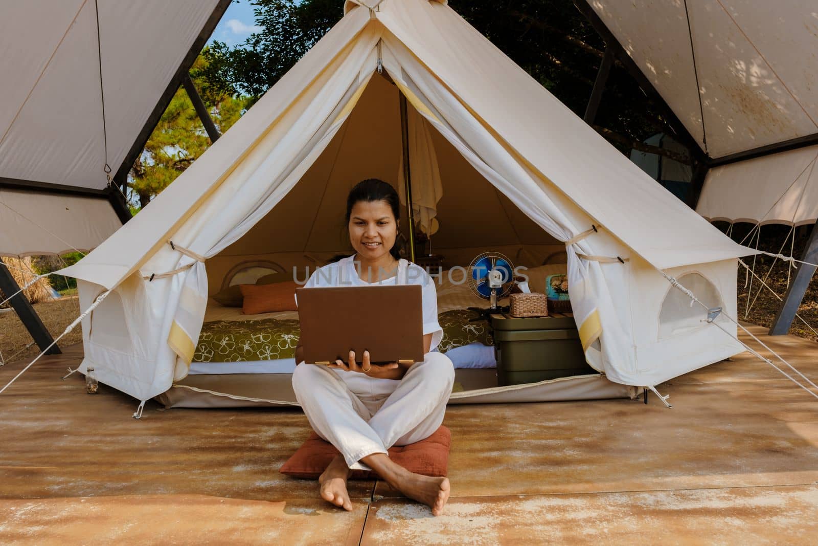 Young woman freelancer traveler working online using a laptop and enjoying the beautiful natural landscape in front of a tent. Digital nomad working on a laptop, remote working