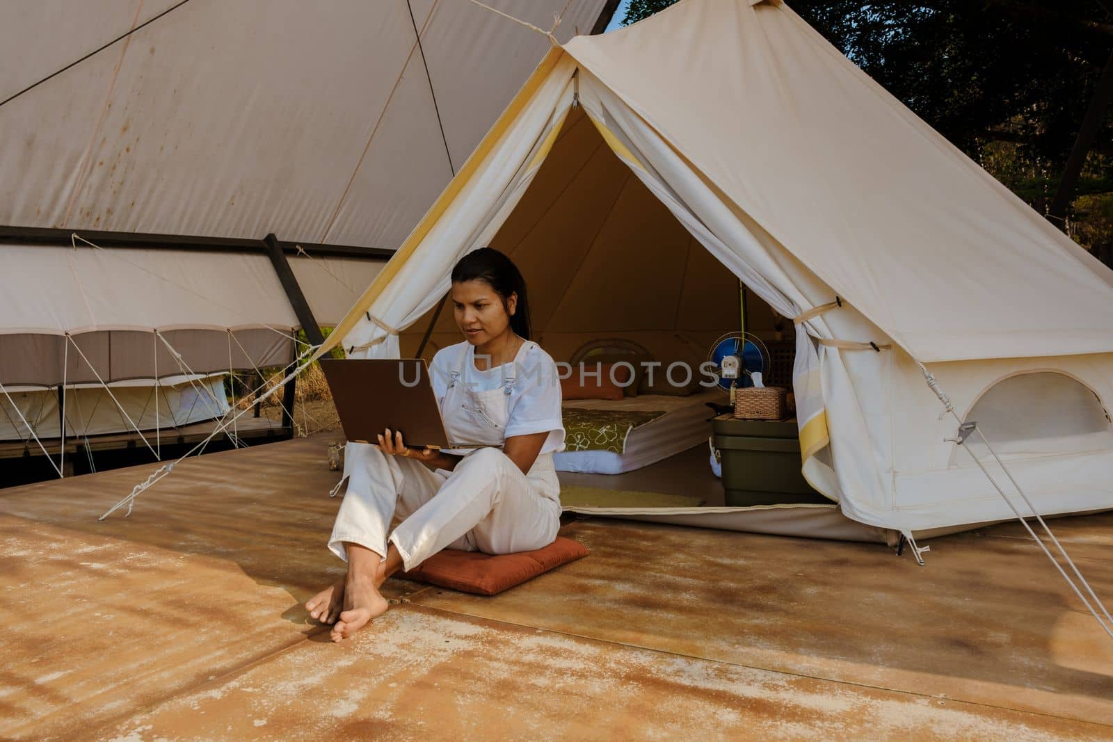 Young Asian woman freelancer working online using a laptop in front of a tent in the mountains by fokkebok