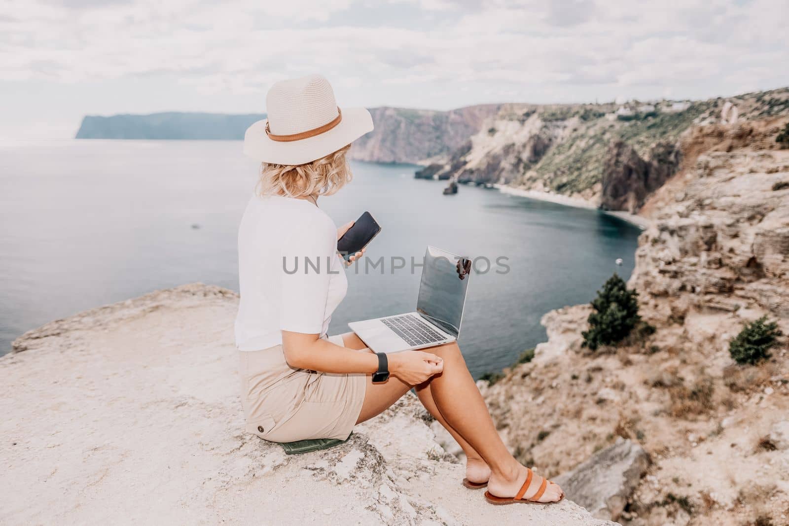 Digital nomad, Business woman working on laptop by the sea. Pretty lady typing on computer by the sea at sunset, makes a business transaction online from a distance. Freelance, remote work on vacation by panophotograph