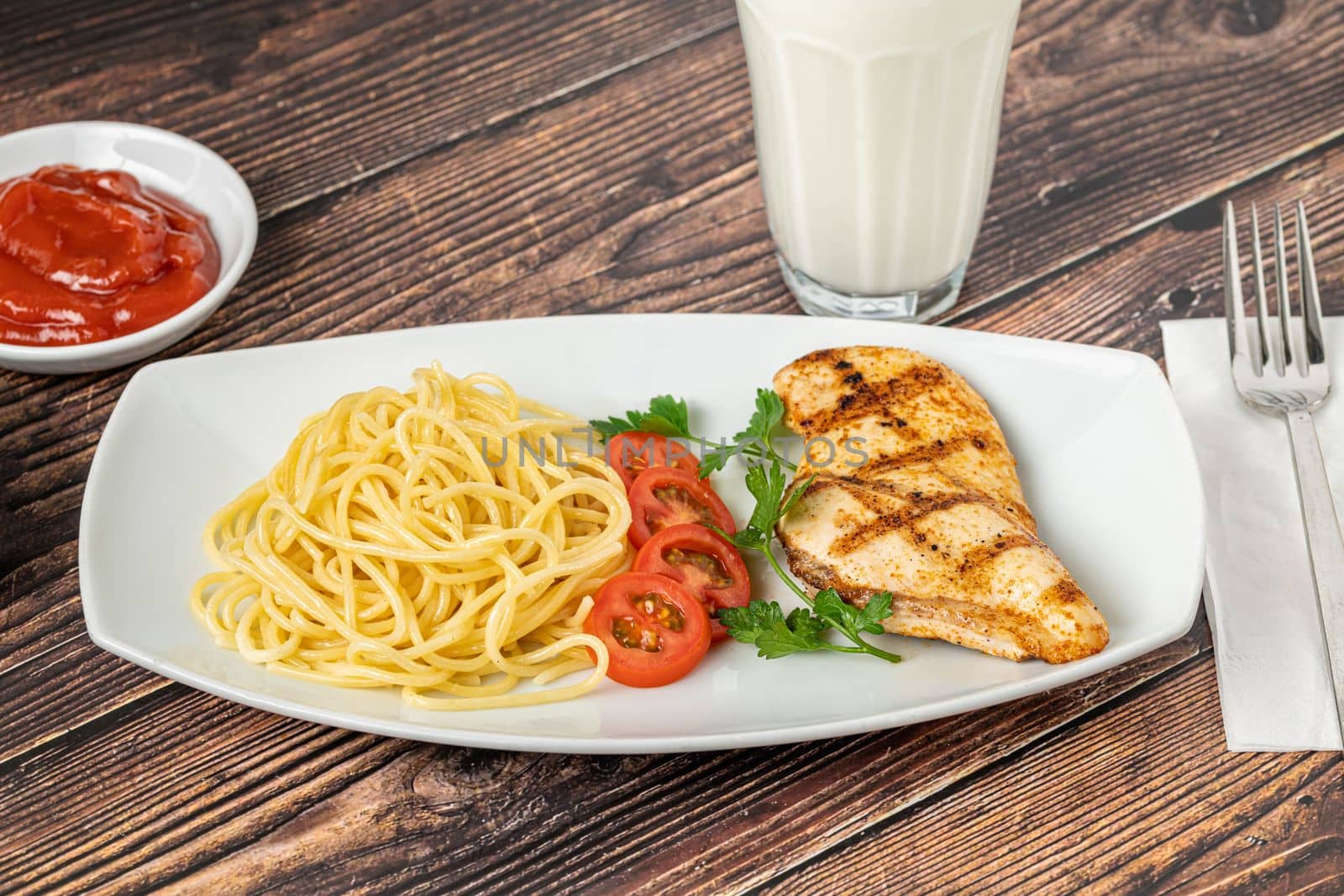 Spaghetti and grilled chicken on a white porcelain plate with buttermilk and sauces on wooden table