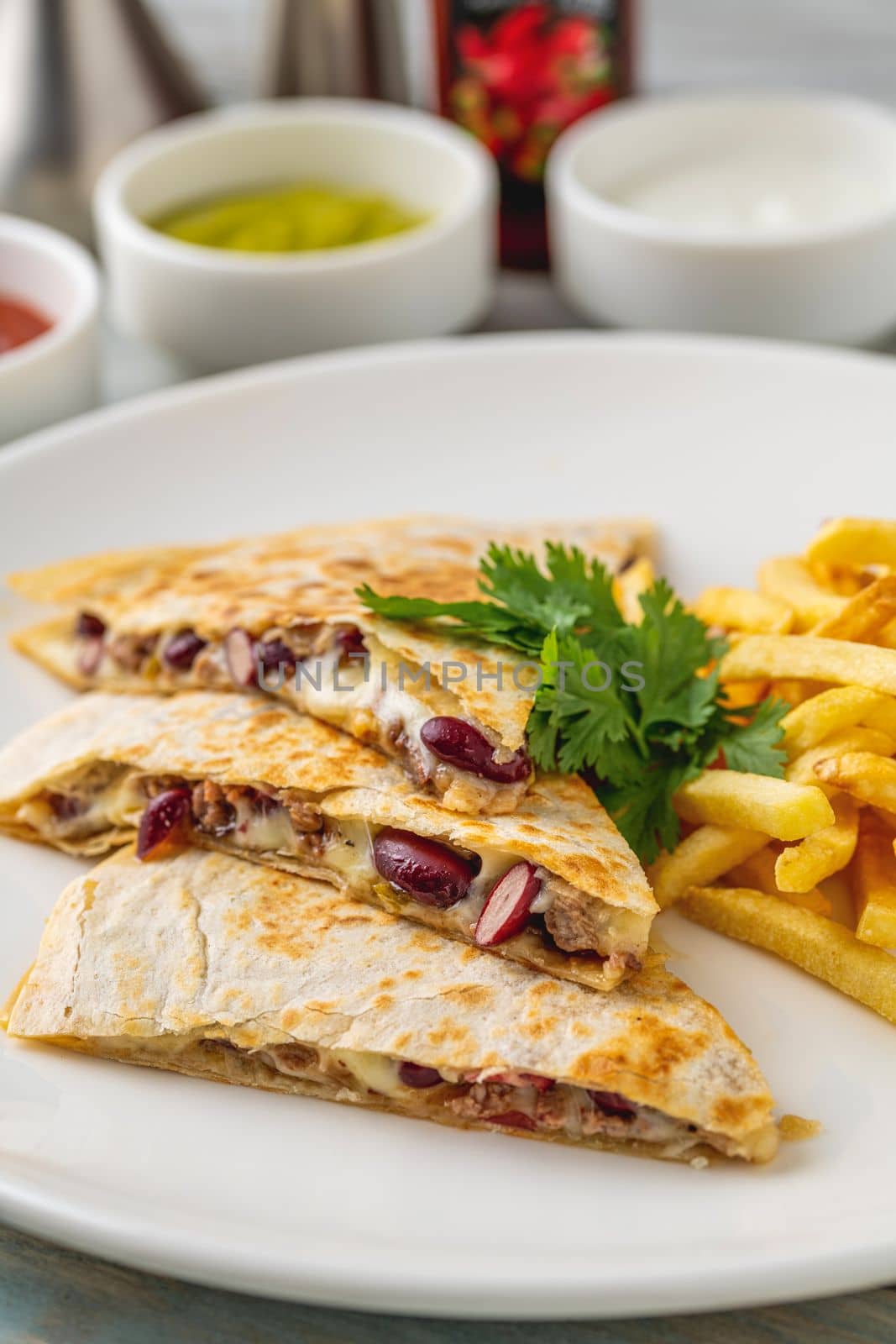 Mexican quesadilla with sauce and french fries on a white porcelain plate by Sonat