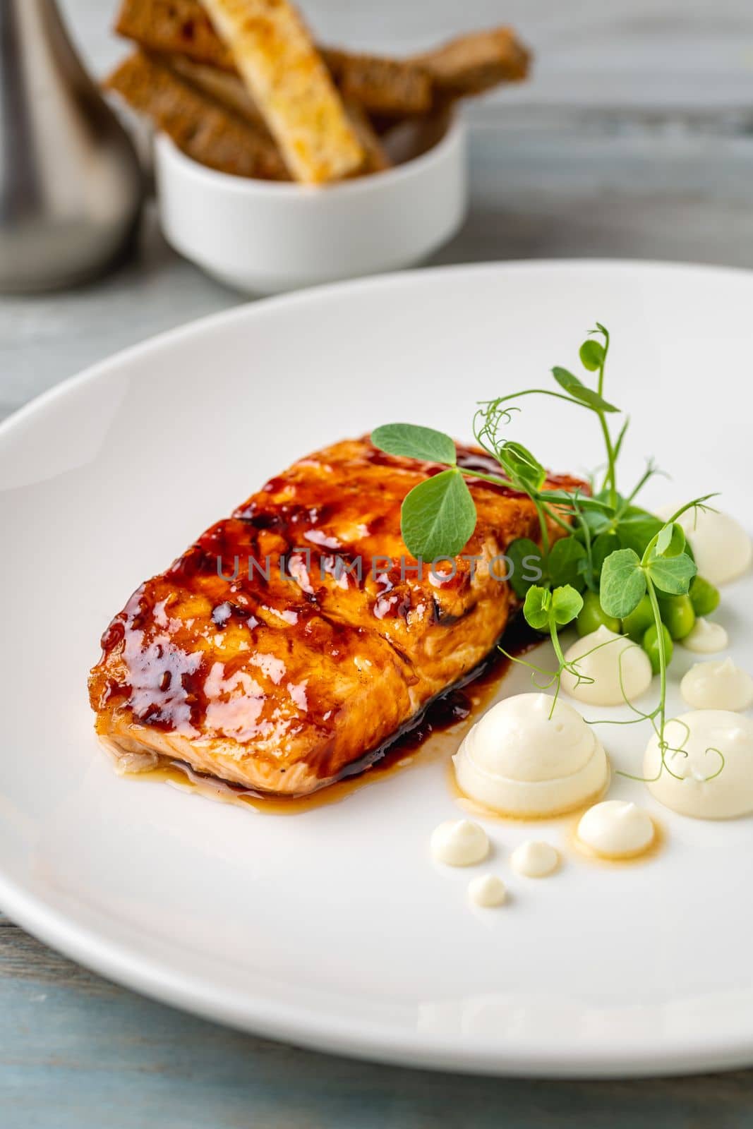 Grilled salmon fillet with sauces next to it on a white porcelain plate by Sonat