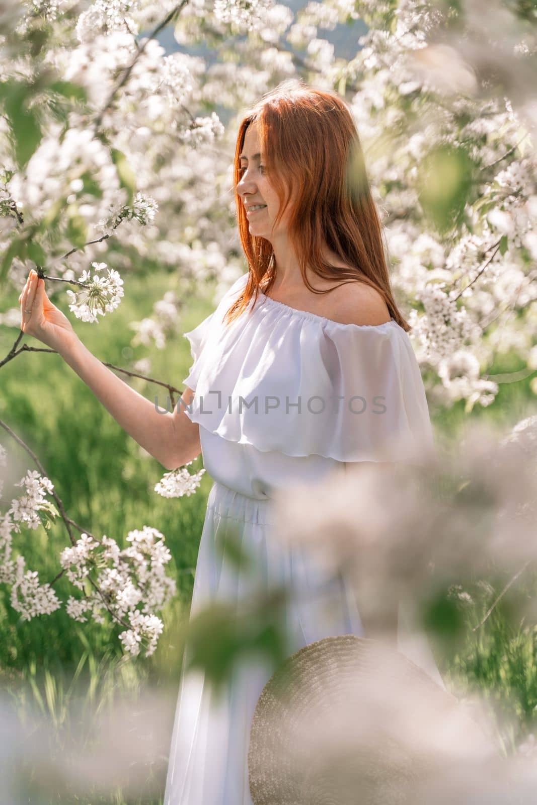 Woman cherry orchard. A happy woman in a long white long dress walks through the green spring blooming cherry garden. Happy cheerful princess bride. The fabric of the skirt flutters in the wind