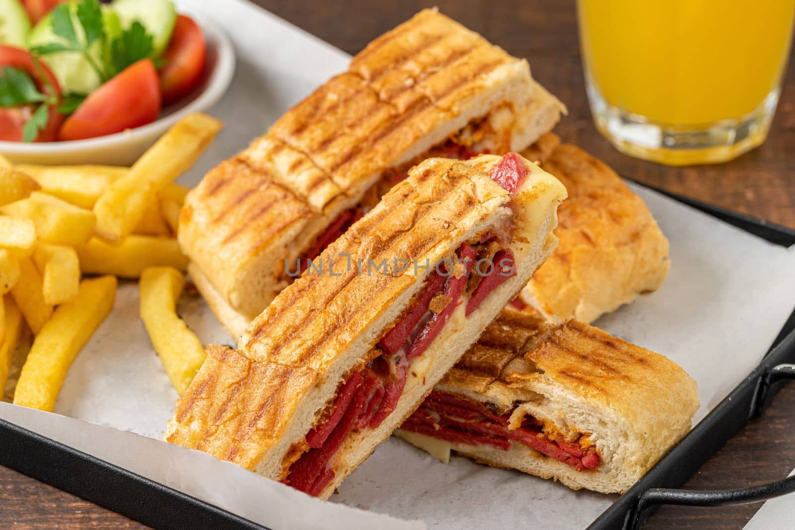 Toast with cheddar cheese and turkish sausage with french fries and salad on wooden table by Sonat