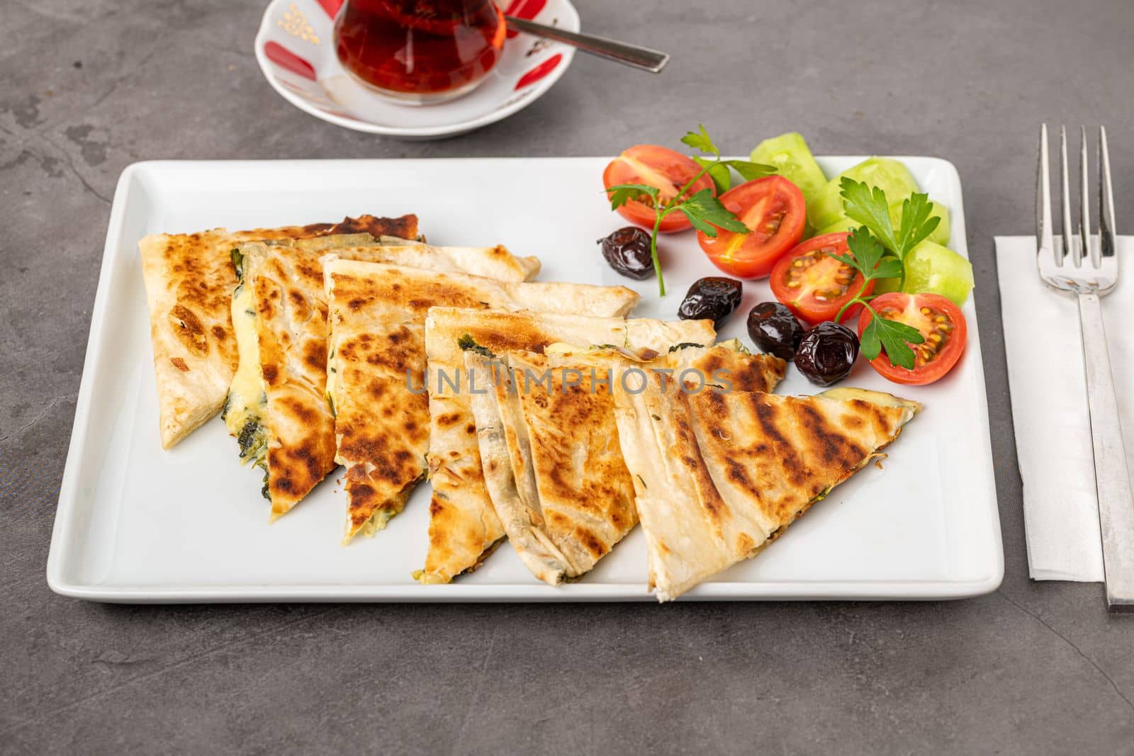 Traditional Turkish flatbread or Gozleme with tomatoes, olives and tea on dark stone table by Sonat